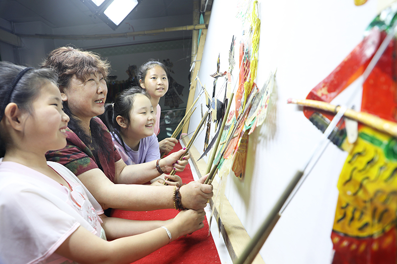 皮影藝人指導小朋友表演皮影戲。